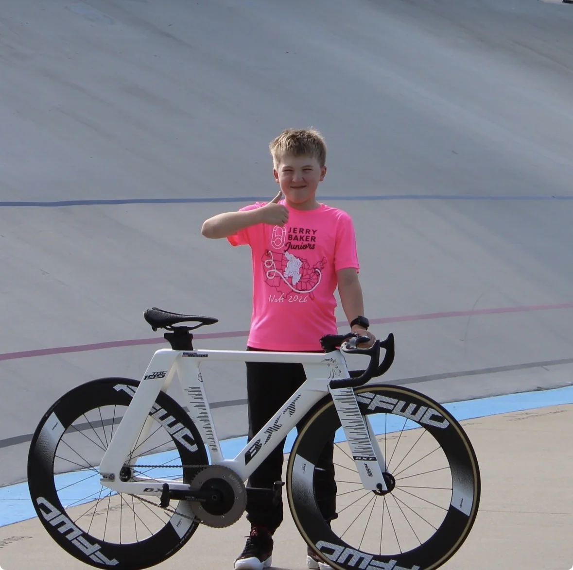 Leo Wilssens giving a thumbs-up beside his white track bike on the velodrome